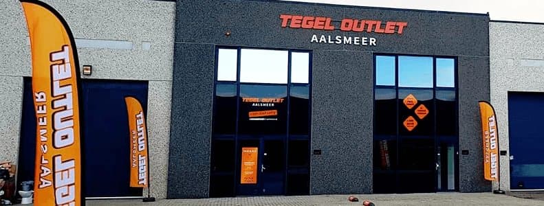 De voorgevel van Tegel Outlet Aalsmeer met oranje vlaggen bij de ingang